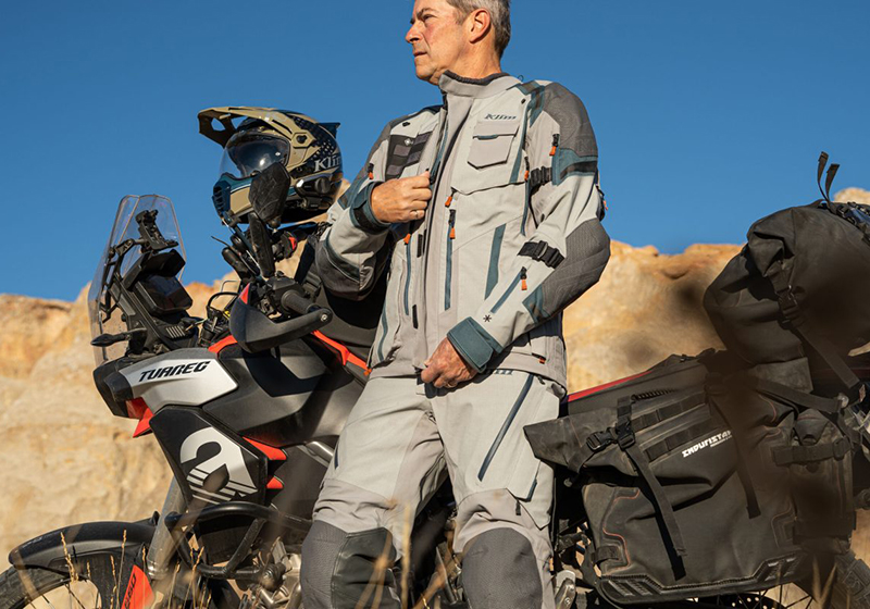 Guy wearing Klim Badlands suit next to Aprilia Tuareg